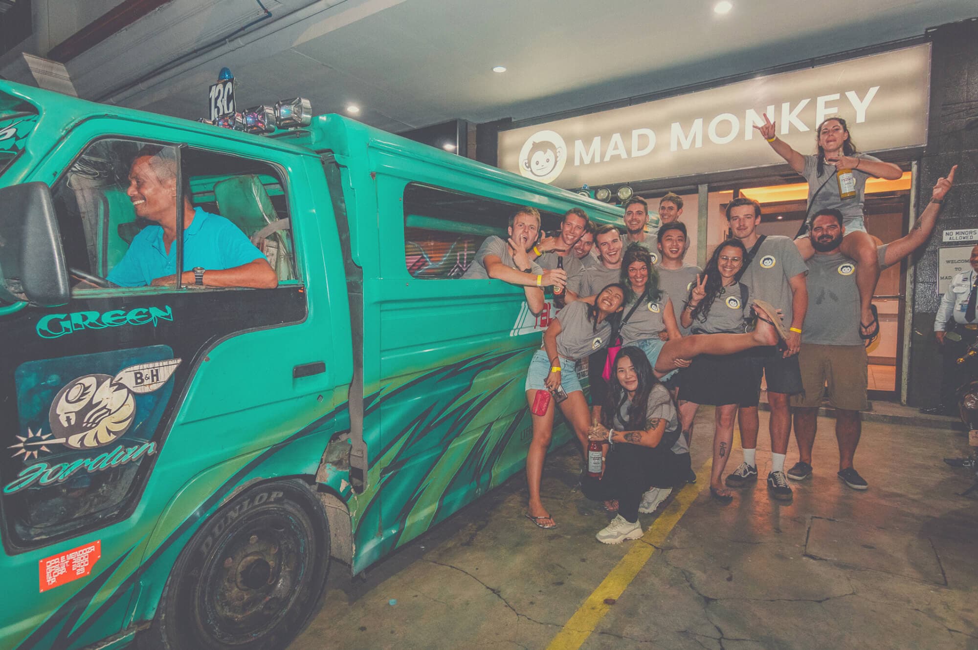Guests and staff crowded around a green jeepney outside a Mad Monkey hostel